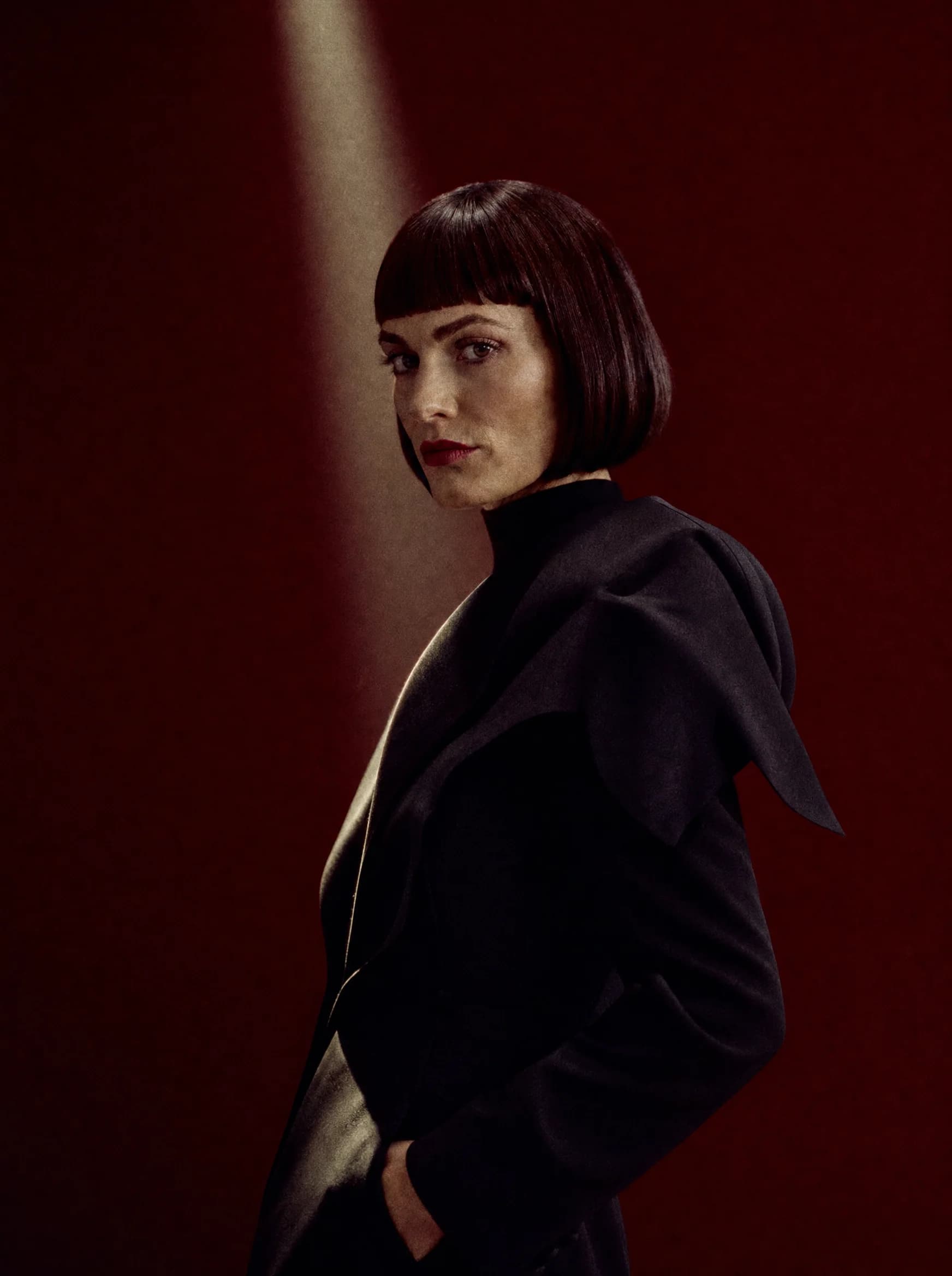 Waist-up editorial portrait of the Atelier Laura creative director against an oxblood backdrop